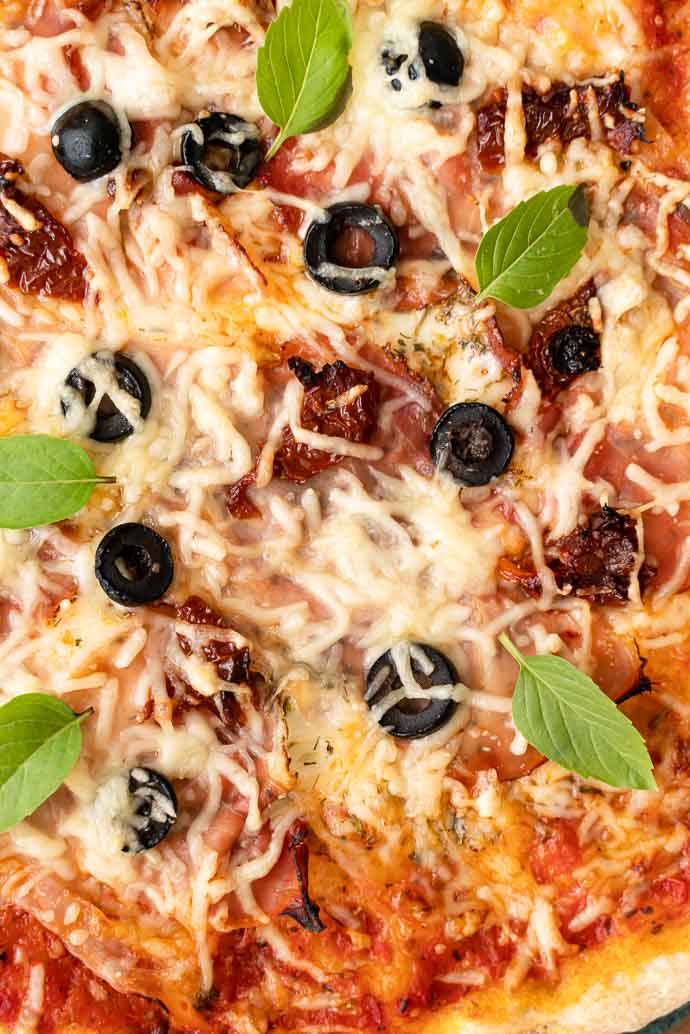 Recette de pizza au speck, base tomates olives & câpres, mozzarella et basilic